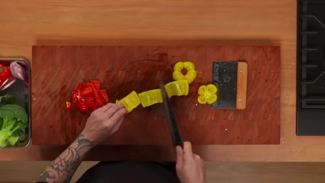 A chef slices a yellow bell pepper into uniform strips for a salad
