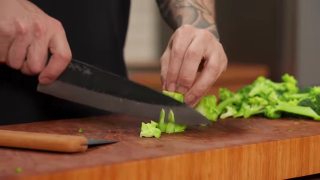 A chef peels the woody outer layer from a broccoli stem before slicing
