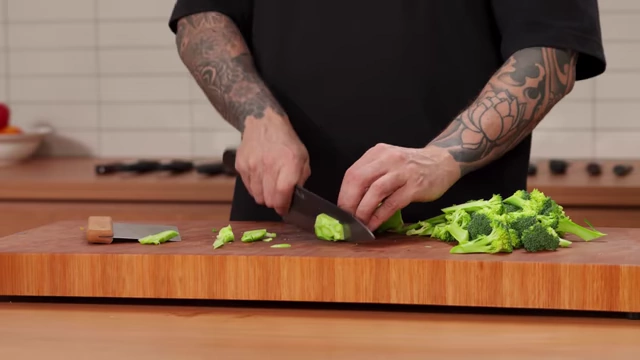 A chef slices a broccoli stem into thin, even pieces for stir-frying