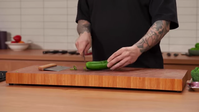 A chef halves a cucumber lengthwise on a cutting board
