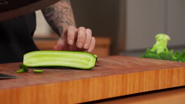 A chef halves a cucumber lengthwise, showing the seeded interior