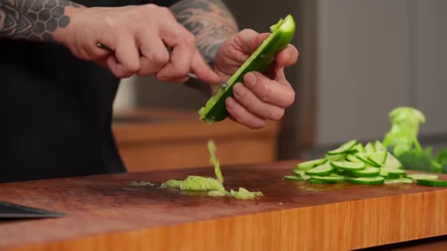 A chef uses a spoon to scoop out the watery seeds from a cucumber half