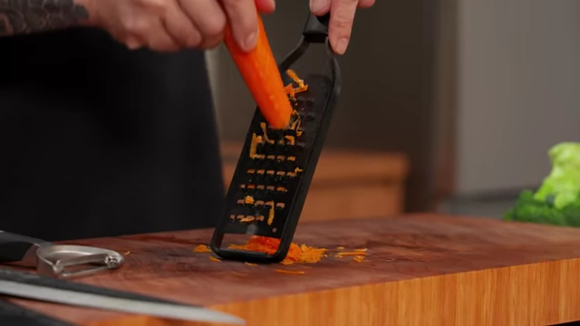 A chef grates a carrot over a cutting board