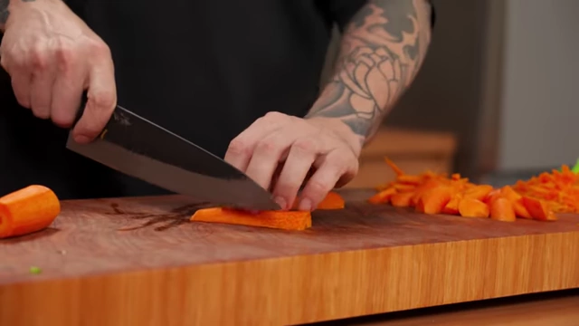A chef slices a carrot diagonally into thick, even pieces for stir-frying