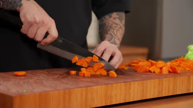 A chef dices a quartered carrot into small, uniform cubes