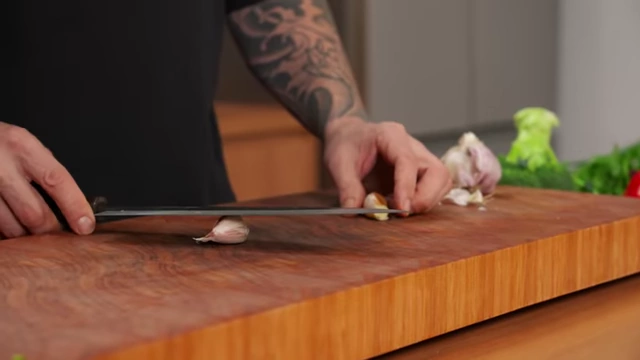 A chef smashes a garlic clove with the flat side of a knife to loosen the skin