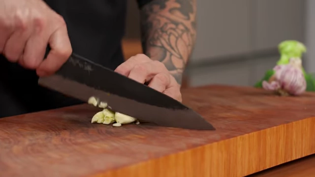 A chef minces garlic cloves using a rocking motion with a chef's knife