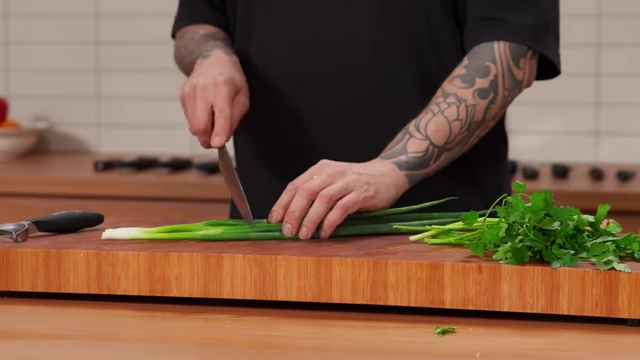 A chef slices the white portion of spring onions into small pieces
