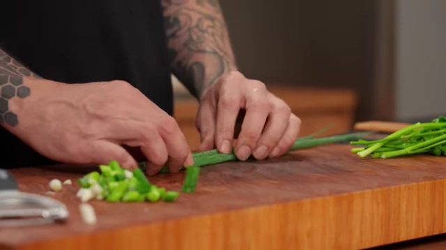 A chef tightly rolls the green parts of spring onions before slicing them