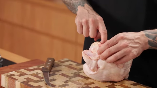 A chef points to the wishbone area in the neck cavity of a raw chicken
