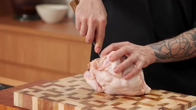 A chef uses a boning knife to scrape flesh away from the wishbone inside a raw chicken