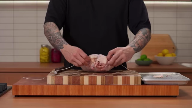 A chef wraps butcher's string around the top of the chicken breasts to secure the wings