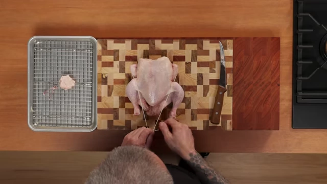 An overhead view of a raw chicken, partially trussed with string