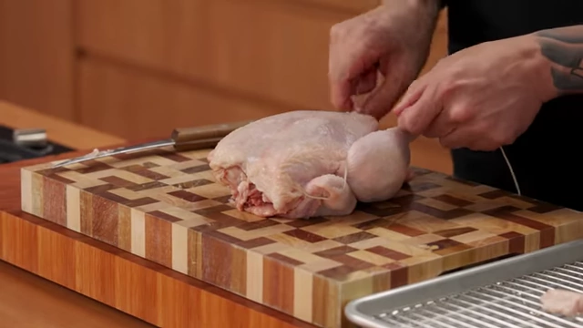 A chef tightens the butcher's string around the drumsticks of a raw chicken to pull them together