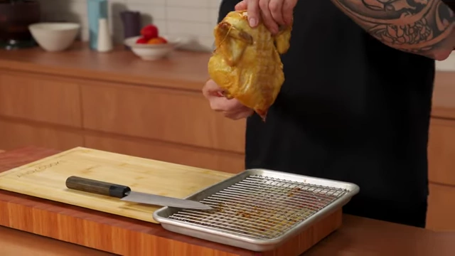 A chef drains excess liquid from the cavity of a roasted chicken into a tray