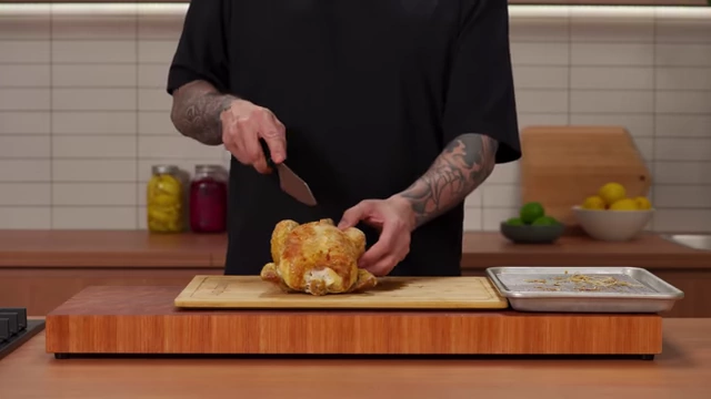 A chef makes an initial cut between the breast and thigh of a roasted chicken
