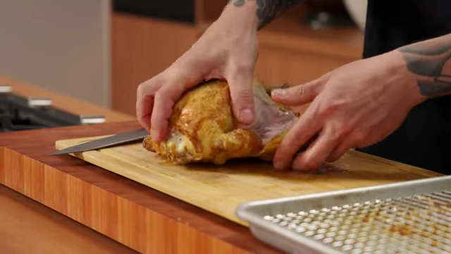 A chef cuts through the joint to remove the leg from a roasted chicken