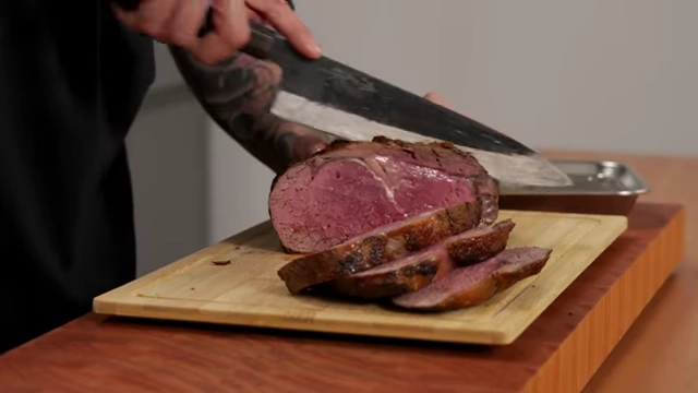 A chef demonstrates slicing roast beef with a sharp knife, letting the blade do the work for clean cuts