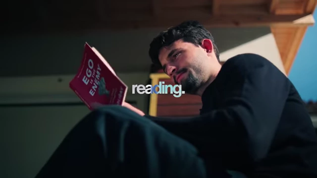 Man reading a book titled "Ego is the Enemy."