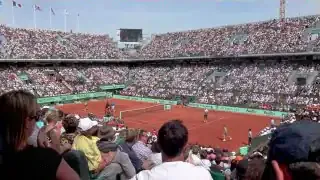 A tennis match in progress at the French Open, with stands full of spectators.