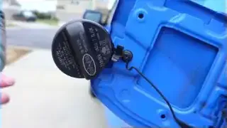 The user demonstrates how to hang the gas cap in the designated holder on the fuel door