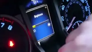 A finger adjusts the brightness slider on the multi-information display using the odometer button