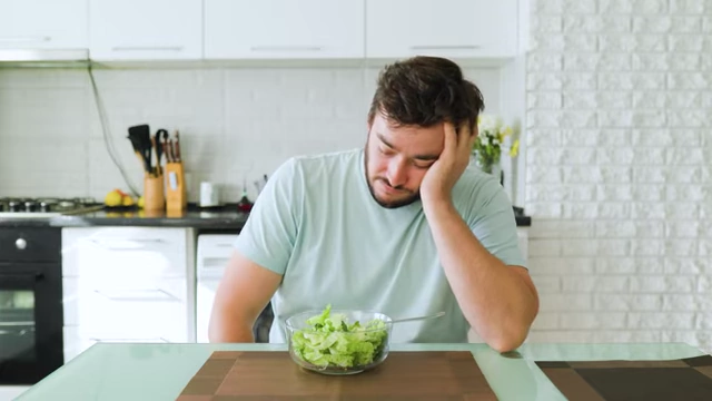 A person sitting at a table with a small salad, looking unenthusiastic and fatigued, symbolizing food aversion due to over-suppression