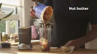 A person preparing a smoothie with various ingredients including nut butter.