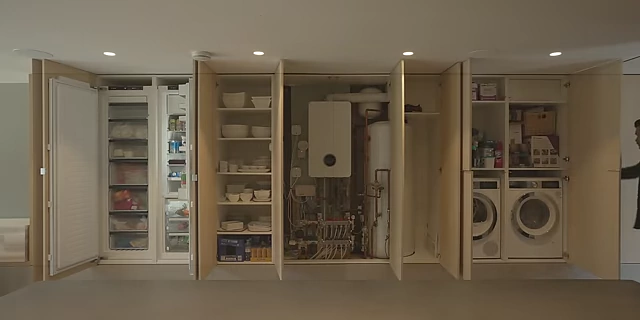 Integrated wall cabinetry that conceals various household essentials, including a refrigerator, pantry, and laundry appliances.