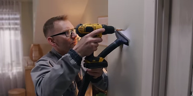 A person using a drill to install a fixture on a wall, with a dust collection attachment.