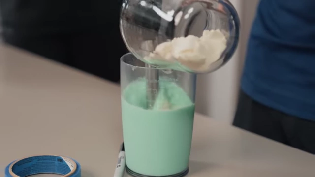 Nick pours protein powder into the liquid base for the high-protein mint chocolate chip recipe.