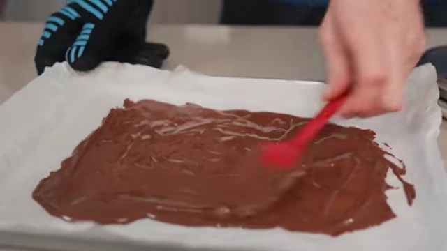 Melted chocolate being spread thinly on parchment paper to cool for mix-ins.