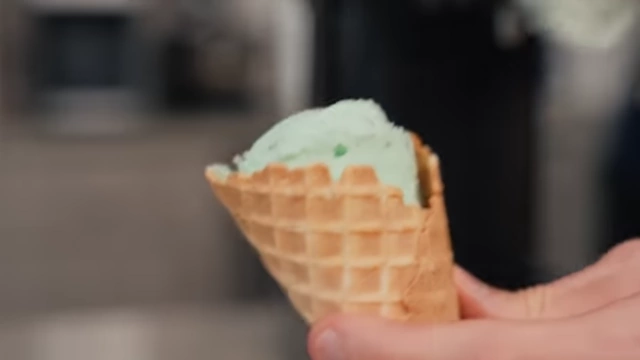 A scoop of mint chocolate chip ice cream in a waffle cone, ready for tasting.