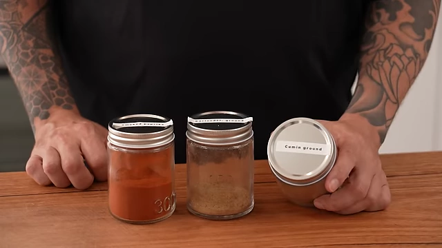 The 'Holy Trinity' of spices: smoked paprika, ground coriander, and ground cumin, presented in small glass jars, essential for earthy and smoky flavors.