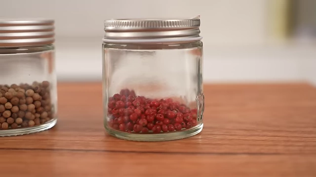 Small glass jars containing black peppercorns and vibrant pink peppercorns, highlighting essential and luxury pepper varieties.