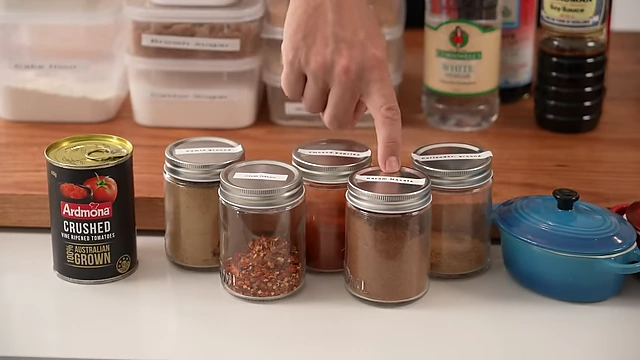 Five essential spices for a beginner's pantry: ground cumin, chili flakes, smoked paprika, garam masala, and ground coriander, displayed in small jars.