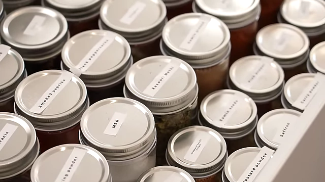 An organized spice drawer featuring a wide array of labeled spice jars, including MSG, smoked paprika, black peppercorns, cumin seeds, and saffron.