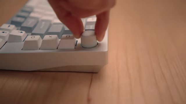 A hand turning a knob on a white mechanical keyboard, demonstrating its customization.