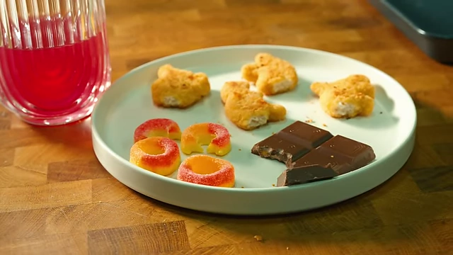A plate showcasing MN's entire restrictive diet, including dinosaur chicken nuggets, gummies, a chocolate bar, and a glass of 3% juice.