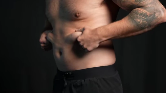 A person pinching the soft outer layer of belly fat, visually representing Layer 1 that hides ab definition.