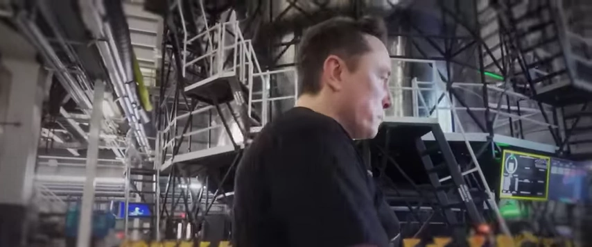 Elon Musk在特斯拉工厂内，走过复杂的工业设备。