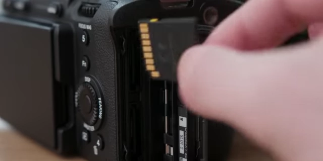 A hand inserting an SD card into a Sony FX3.