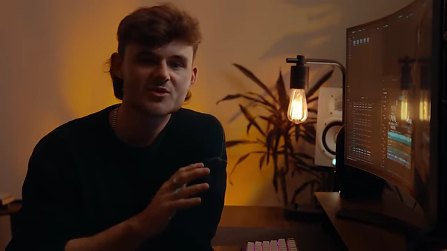 Mitchell Mullins, the speaker, talks at his desk with a large monitor displaying editing software in the background.
