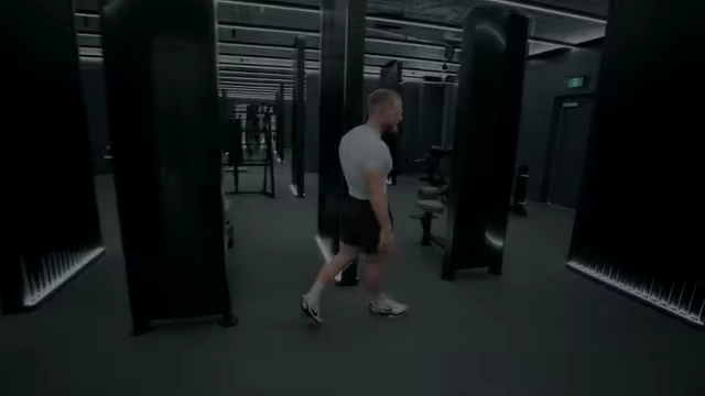 Jeff Nippard walking into the dark-toned gym, which features dramatic lighting and bodybuilding-focused equipment.