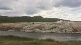 A panoramic view of the Yellowstone National Park landscape, featuring a river and geothermal activity.
