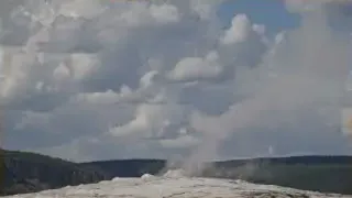 Old Faithful geyser erupting in Yellowstone National Park under a blue sky with scattered clouds.