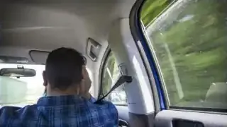 A person sitting in a car with a single rear window open, illustrating the phenomenon of Helmholtz resonance.