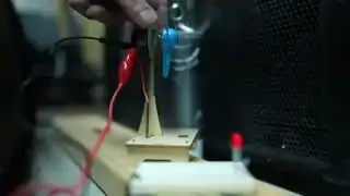 A close-up of a small fan blowing air onto a Christmas ornament attached to wires, illustrating a Helmholtz resonance experiment.