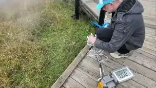 The speaker setting up a seismograph outdoors on a wooden walkway near a geothermal feature.