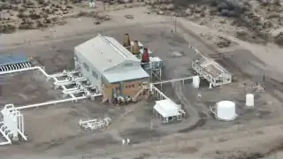 An aerial view of an industrial power plant with multiple buildings and pipelines in a desert landscape.